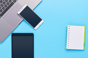 top view upon gadgets on blue background, the composition of a laptop, white headphones, phone, glass with a drink and car keys