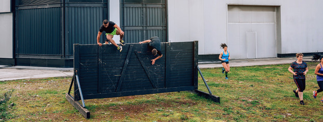 Group of participants in an obstacle course running and climbing a wall