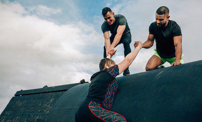 Female participant in an obstacle course climbing a drum helped by her teammates