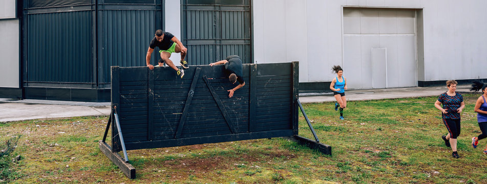 Group of participants in an obstacle course running and climbing a wall