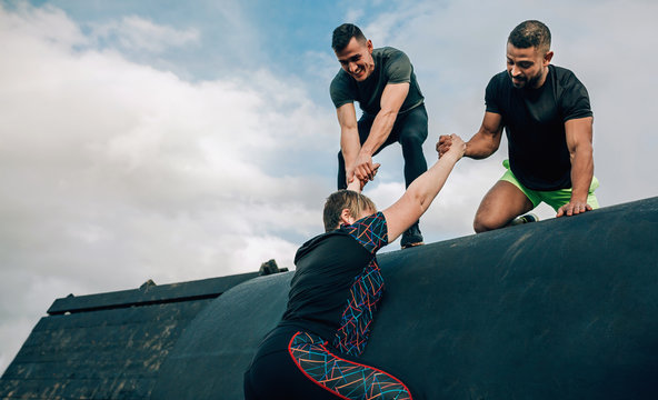 Female participant in an obstacle course climbing a drum helped by her teammates - Powered by Adobe