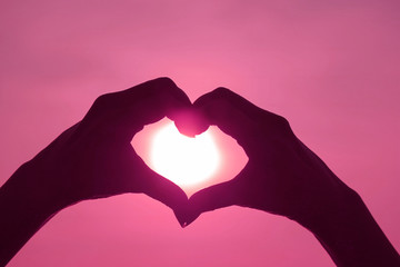 Obraz premium Pink Colored silhouette of female's hand posing LOVE HEART sign against shiny sun