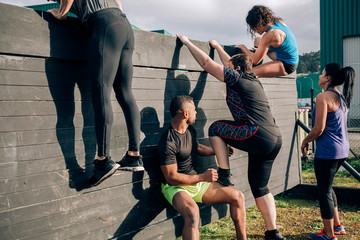 Group of participants in an obstacle course climbing a wall - obrazy, fototapety, plakaty