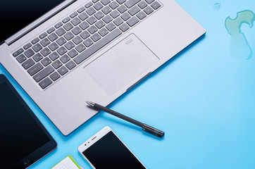 top view upon gadgets on blue background, the composition of a laptop, white headphones, phone, glass with a drink and car keys