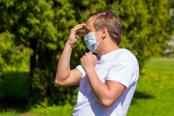 a man in a mask from allergy, in a white T-shirt, stands in the park