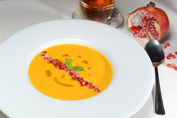 pumpkin cream soup on a white plate decorated with pomegranate seeds and spices