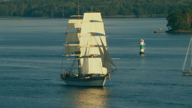 A majestic two-masted tall ship sails upstream to return to port after cruising the ocean.