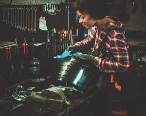 Obraz na płótnie Canvas African american woman mechanic polishing motorcycle fuel tank