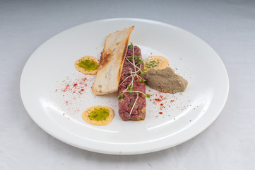 veal tartare with pate and microgreen on a white plate on a pure white background