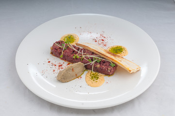 veal tartare with pate and microgreen on a white plate on a pure white background