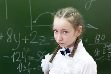 Schoolgirl teenager sad at the school blackboard. Girl student 10-12 years of age in sadness sad...