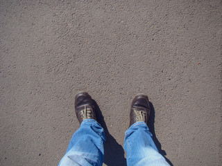 Fototapeta premium Top view on brown boots, green laces, blue jeans. Background - asphalt.