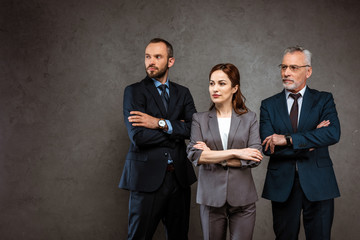 successful businesswoman and handsome businessmen standing with crossed arms on grey