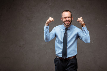happy businessman in suit gesturing while celebrating on grey