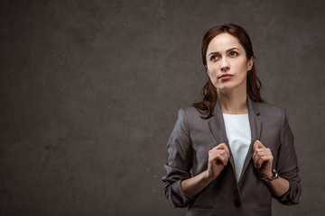 thoughtful brunette businesswoman in formal wear standing on grey