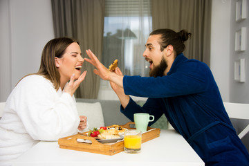 beautiful young couple having breakfast in bath robe, blond attractive size plus female model and bearded male model