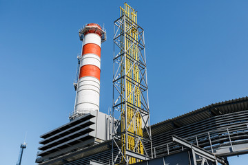 Gas turbine power plant on natural gas with chimneys of red-white color against a blue sky on a sunny day