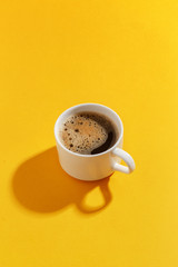 A cup of black coffee on a yellow background.