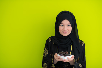 modern muslim woman holding a plate of dates in ramadan kareem on green background