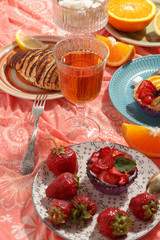 Appetizing breakfast, orange, croissant, strawberries and cakes on a red tablecloth. Top view.