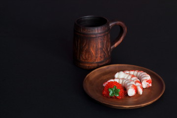 Ceramic mug and clay plate with shrimps and red caviar on black background. Concept — restaurant, menu. Play of light and shadow. Minimal style.