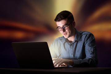 Young handsome businessman working late at night in the office with warm lights in the background