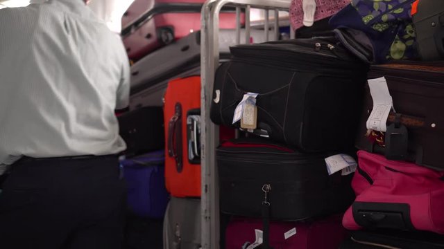 Luggage trolleys with a large pile of suitcases and loaders passing by
