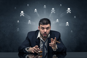 Loser drunk man sitting at table with skulls concept around
