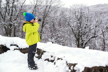 Fototapeta na wymiar Сute kid nature explorer in winter forest. Little boy binoculars explorer at winter nature. Winter vacation.