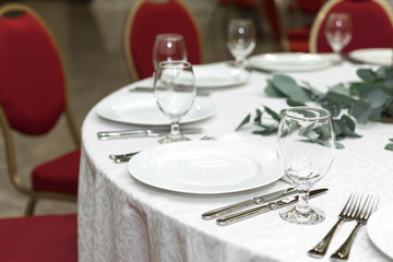 Festively decorated round banquet table in the restaurant. Fresh flowers are golden candles and red chairs. expensively rich