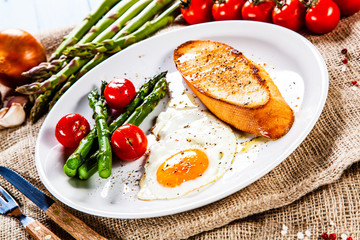 Fried egg with vegetables and toast on wooden table