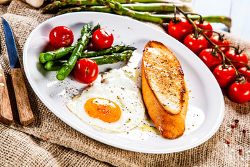 Fried egg with vegetables and toast on wooden table