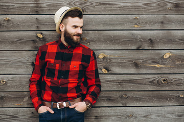 Portrait of a young stylish bearded man dressed up in jeans and a true worker black by red shirt on a wooden background.