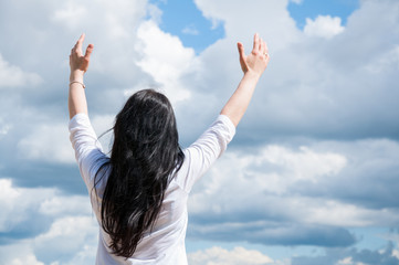 a woman with her arms raised praises God or prays. Against the blue sky and white clouds