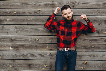 Portrait of a young stylish bearded man dressed up in jeans and a true worker black by red shirt on...