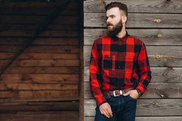 Portrait of a young stylish bearded man dressed up in jeans and a true worker black by red shirt on...