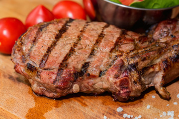 Close up freshly grilled bone steak on wood and fresh salad in bowl