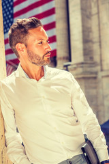 Thinking outside. Young European Businessman with beard, wearing white shirt, holding briefcase, standing outside office building on street in New York City, under sunshine, looking, thinking. .