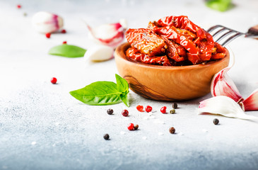 Sun dried tomatoes in olive oil with green basil and spices in wooden bowl on gray kitchen table, place for text