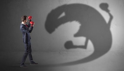 Businessman with boxing glove fighting with a big monster shadow

