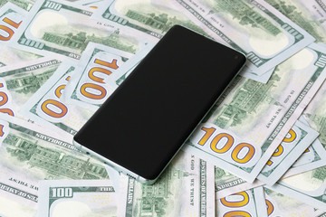 Mobile phone on the background of many hundred dollar banknotes 