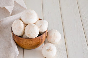 Fresh raw champignons in a wooden bowl on a white background with space for text.