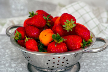 Strawberries and apricots in a colander on the table.