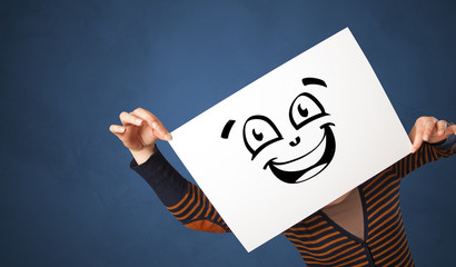 Casual person holding a paper in front of his face with drawn emoticon face 