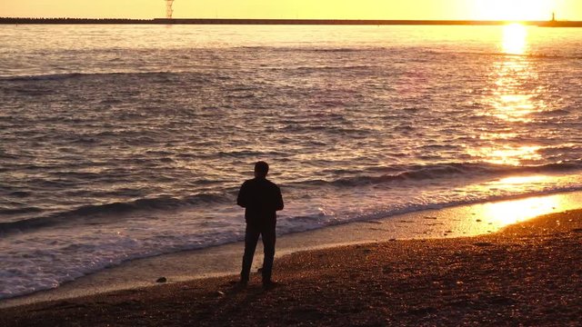 A man throws stones into the sea at sunset. The traditional throwing of stones into the water. The sea and the man at sunset