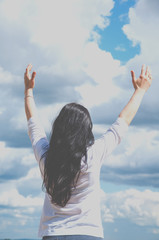 a woman with her arms raised praises God or prays. Against the blue sky and white clouds