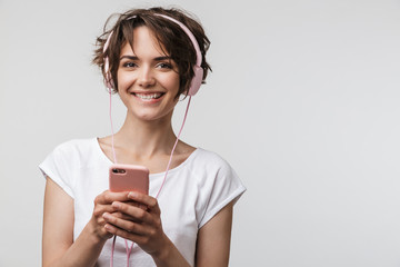 Image of optimistic woman in basic t-shirt holding smartphone while listening to music with...