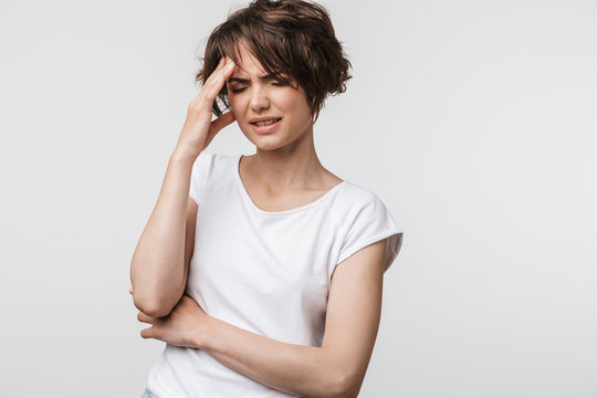 Photo of stressed woman with short brown hair in basic t-shirt grabbing her head and rubbing temples because of headache