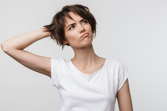 Portrait of young woman with short brown hair in basic t-shirt frowning and looking upward