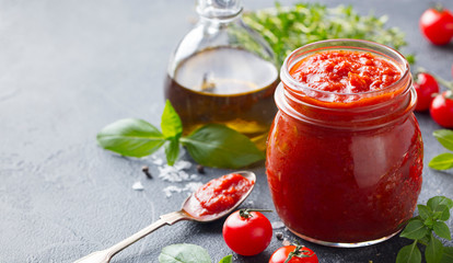 Traditional tomato sauce in a glass jar with fresh herbs, tomatoes and olive oil. Copy space. Slate...